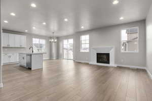 Kitchen with sink, decorative light fixtures, a center island with sink, white cabinets, and light wood-type flooring