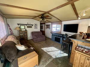 Living room with lofted ceiling with beams, dark colored carpet, and ceiling fan