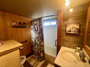 Full bathroom with wooden walls, vanity, shower / tub combo, and toilet