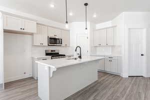 Kitchen featuring a center island with sink, hanging light fixtures, stainless steel appliances, white cabinets, and sink