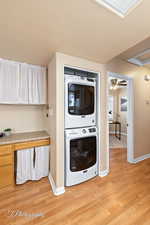 Clothes washing area featuring ceiling fan, light hardwood / wood-style floors, and stacked washer and clothes dryer