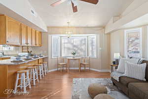 Living room featuring ceiling fan with notable chandelier, sink, light wood-type flooring, and a textured ceiling