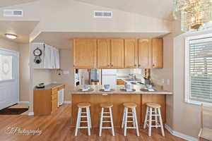 Kitchen featuring kitchen peninsula, sink, white refrigerator, light hardwood / wood-style floors, and lofted ceiling