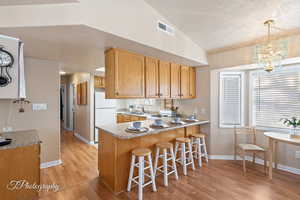 Kitchen with sink, kitchen peninsula, white fridge, vaulted ceiling, and decorative light fixtures