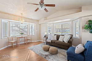 Living room with a textured ceiling, ceiling fan with notable chandelier, light hardwood / wood-style floors, and lofted ceiling