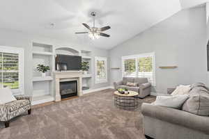 Living room featuring carpet, built in shelves, vaulted ceiling, and ceiling fan