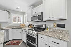 Kitchen with light stone counters, white cabinets, appliances with stainless steel finishes, and sink