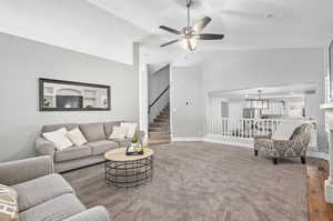 Living room with ceiling fan with notable chandelier, carpet, and high vaulted ceiling