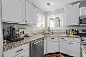 Kitchen featuring light stone counters, sink, stainless steel appliances, and white cabinets