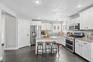 Kitchen featuring a breakfast bar area, white cabinetry, a kitchen island, appliances with stainless steel finishes, and light stone countertops