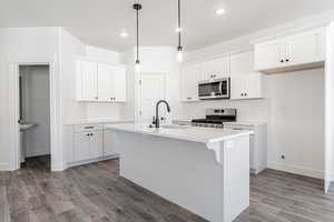 Kitchen featuring appliances with stainless steel finishes, sink, white cabinetry, and an island with sink