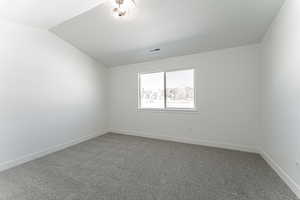 Carpeted empty room with vaulted ceiling and a textured ceiling