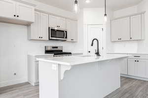 Kitchen with sink, decorative light fixtures, an island with sink, stainless steel appliances, and white cabinets