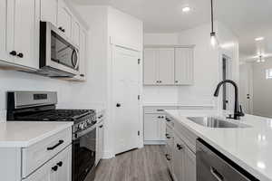 Kitchen featuring sink, appliances with stainless steel finishes, white cabinetry, light stone countertops, and decorative light fixtures