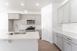 Kitchen featuring appliances with stainless steel finishes, light hardwood / wood-style flooring, decorative light fixtures, gray cabinets, and sink