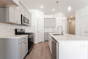 Kitchen with gray cabinetry, stainless steel appliances, decorative light fixtures, light hardwood / wood-style floors, and sink