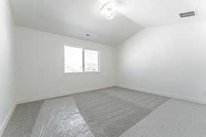 Carpeted spare room featuring lofted ceiling