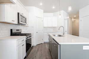 Kitchen with appliances with stainless steel finishes, decorative light fixtures, sink, and white cabinets