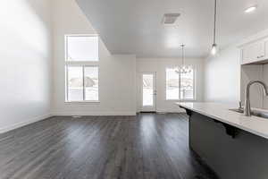 Kitchen with white cabinetry, hanging light fixtures, a notable chandelier, sink, and dark wood-type flooring