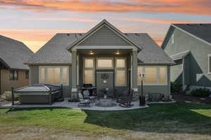 Back house at dusk featuring a hot tub, a yard, and a patio area