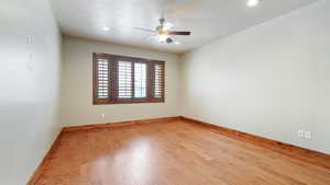 Empty room featuring a textured ceiling, a ceiling fan, hardwood / wood-style flooring, and baseboards