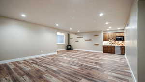 Unfurnished living room featuring recessed lighting, visible vents, a wood stove, light wood-type flooring, and baseboards