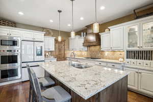 Kitchen with stainless steel appliances, sink, pendant lighting, white cabinetry, and a center island with sink