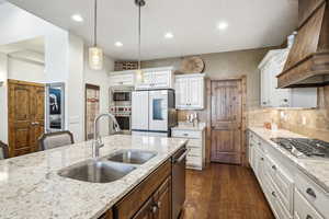 Kitchen with pendant lighting, sink, white cabinetry, stainless steel appliances, and dark hardwood / wood-style floors