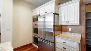 Kitchen with dark wood finished floors, appliances with stainless steel finishes, white cabinetry, light stone countertops, and baseboards