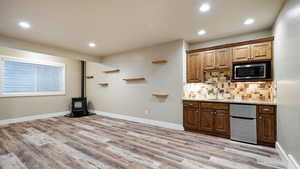 Kitchen featuring light wood-style floors, stainless steel microwave, a wood stove, and decorative backsplash