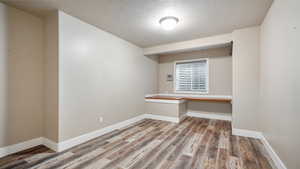 Unfurnished room with a textured ceiling, built in desk, wood finished floors, and baseboards