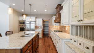 Kitchen with a sink, appliances with stainless steel finishes, a center island with sink, glass insert cabinets, and pendant lighting