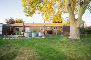 Rear view of house with a trampoline, a lawn, and central AC