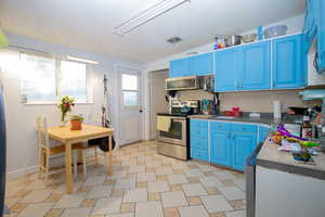 Kitchen with appliances with stainless steel finishes, backsplash, lofted ceiling, and blue cabinetry