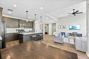 Kitchen with decorative light fixtures, a kitchen island with sink, appliances with stainless steel finishes, a breakfast bar area, and light hardwood / wood-style floors