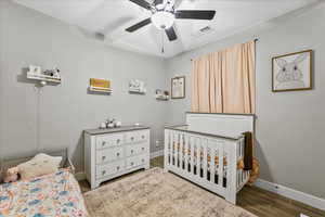 Bedroom with dark hardwood / wood-style flooring, ceiling fan, and a nursery area