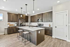 Kitchen with light hardwood / wood-style flooring, stainless steel appliances, hanging light fixtures, and sink