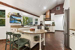 Kitchen featuring a brick wall, vaulted ceiling, wood beams and shiplap