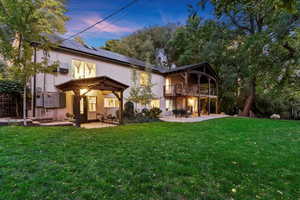 Back house at dusk with a patio, deck, and lawn