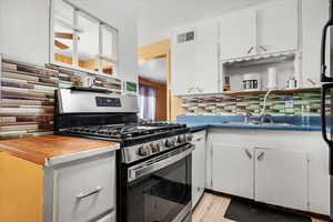 Kitchen featuring white cabinets, backsplash, stainless steel appliances, light hardwood / wood-style flooring, and sink