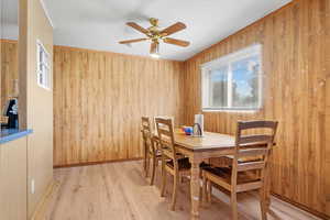 Dining space with wooden walls, light hardwood / wood-style floors, and ceiling fan