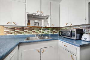 Kitchen featuring decorative backsplash, white cabinetry, white dishwasher, and sink