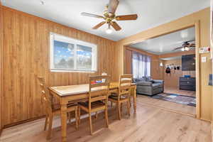 Dining space with light hardwood / wood-style floors, wood walls, and ceiling fan