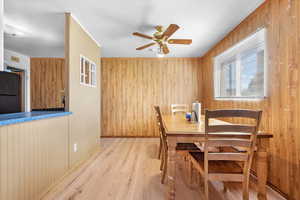 Dining area with wooden walls, light hardwood / wood-style floors, and ceiling fan