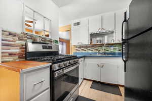 Kitchen featuring decorative backsplash, white cabinetry, black refrigerator, stainless steel range with gas cooktop, and sink