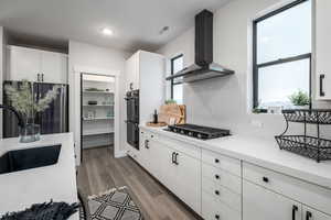 Kitchen with appliances with stainless steel finishes, white cabinetry, dark wood-type flooring, backsplash, and wall chimney range hood