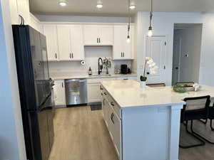 Kitchen with black refrigerator, hanging light fixtures, white cabinetry, and stainless steel dishwasher