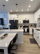 Kitchen featuring white cabinets, sink, decorative light fixtures, stainless steel appliances, and light wood-type flooring