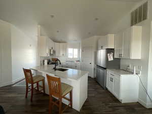 Kitchen with kitchen peninsula, dark wood-type flooring, white cabinetry, appliances with stainless steel finishes, and a breakfast bar area