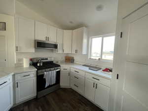 Kitchen featuring vaulted ceiling, appliances with stainless steel finishes, white cabinetry, and dark hardwood / wood-style flooring